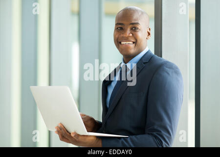 lächelnden jungen afrikanischen Geschäftsmann mit Laptop-Computer im Haus Stockfoto