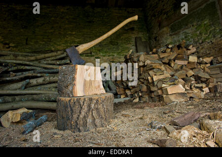 Axt in ein Stück Holz auf der Oberseite ein Hackklotz, einen Haufen von Protokollen und gehacktem Holz stecken. Stockfoto