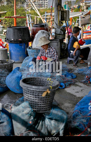 Rollentausch mit Mann fürsorglich für Baby während Frau neigt die Fischernetzen dazu. Thailand S. E. Asien. Stockfoto