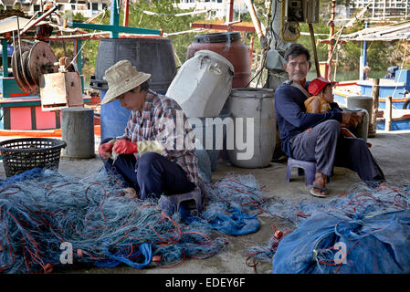 Rollentausch mit Mann fürsorglich für Baby während Frau neigt die Fischernetzen dazu. Thailand S. E. Asien. Stockfoto