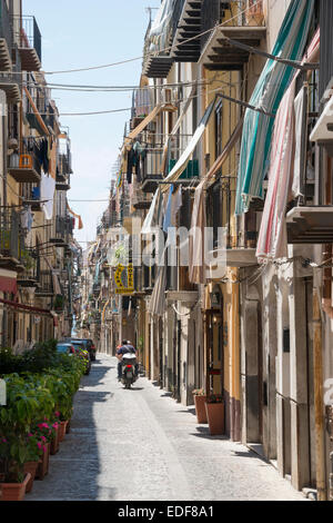 Eine schmale Straße in Cefalù Sizilien Italien mit einem Scooter geritten. Wasch- und Markisen hängen von den Balkonen der Gebäude Stockfoto