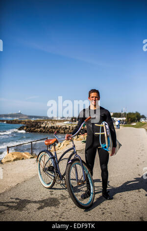 Ein junger Mann posiert mit einem Surfbrett und Cruiser-Fahrrad an der Küste von Kalifornien. Stockfoto