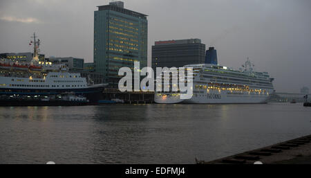 Zwei Kreuzfahrtschiffe vor Anker am Terminal Amsterdam Passagiere in der Abenddämmerung mit Skyline der Stadt im Hintergrund Stockfoto