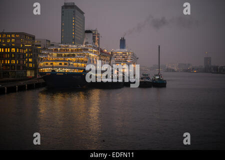 Zwei Kreuzfahrtschiffe vor Anker am Terminal Amsterdam Passagiere in der Abenddämmerung mit Skyline der Stadt im Hintergrund Stockfoto