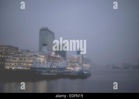 Zwei Kreuzfahrtschiffe vor Anker am Terminal Amsterdam Passagiere in der Abenddämmerung mit Skyline der Stadt im Hintergrund Stockfoto