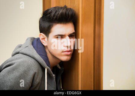 Junger Mann hinter einer Tür mit einem konzentrierten Ausdruck hören versuchen, Dinge zu belauschen Stockfoto