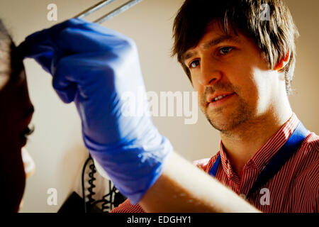 Männlich-NHS-Arzt tragen Schutzhandschuhe, die Untersuchung eines Patienten in einem Krankenzimmer Behandlung Stockfoto