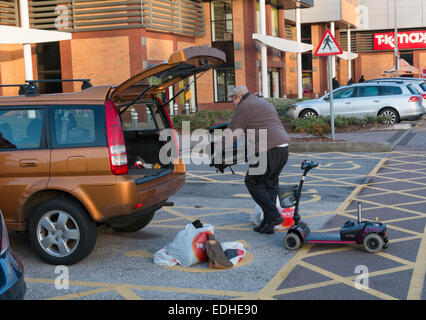 Mann, laden eine behinderte Elektromobil und Taschen in der Rückseite des kleinen Fließheck Auto in einem Parkhaus Einkaufszentrum. Stockfoto