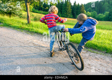 Kinder und ein Fahrrad auf der Landstraße, Kinderfahrradkinder, Landstraßenjunge und -Mädchen am Straßenrand Stockfoto