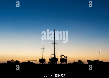 Segelboote auf dem Festland bei Sonnenaufgang im Hafen von Lindisfarne, Holy Island, Northumberland, England. Silhouette Stockfoto