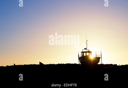 Angelboot/Fischerboot auf dem Festland bei Sonnenaufgang im Hafen von Lindisfarne, Holy Island, Northumberland, England. Silhouette Stockfoto