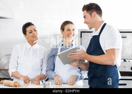 Glückliche Köche diskutieren Rezept auf Digital-Tablette In Küche Stockfoto