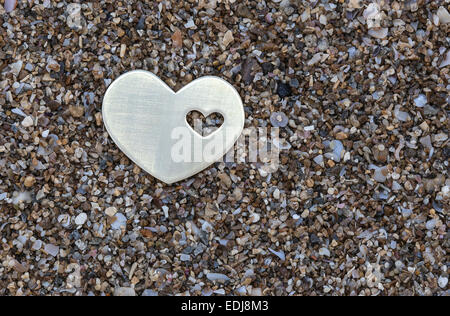 Eine kleine helle metallische Herzform wird auf dunklem Sand gelegt. Stockfoto