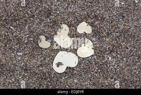 Fünf kleine metallische Herzformen sind auf dunklem Sand gelegt. Stockfoto