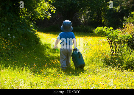 Ein zwei Jahre altes Kind mit einer Gießkanne zu Fuß durch ein Shropshire Garten, England, UK. Stockfoto