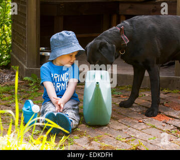 Ein zwei Jahre altes Kind sitzt neben einem Hund trinken aus einer Gießkanne. Stockfoto