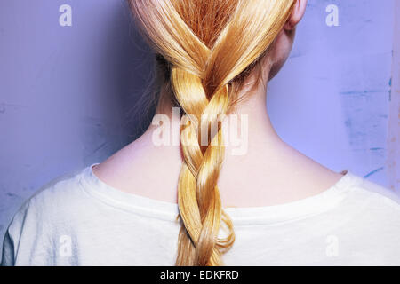 Mädchen mit blonden Haaren, zu einem Zopf auf lila Hintergrund geflochten Stockfoto