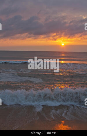 Eine dunkle, unruhige Meer spiegelt die Farben der untergehenden Sonne an einem Strand in der Abenddämmerung Stockfoto