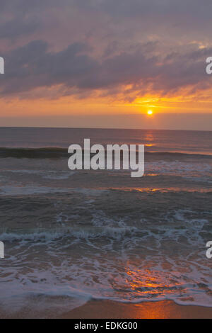 Eine dunkle, unruhige Meer spiegelt die Farben der untergehenden Sonne an einem Strand in der Abenddämmerung Stockfoto