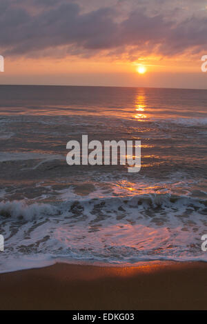 Eine dunkle, unruhige Meer spiegelt die Farben der untergehenden Sonne an einem Strand in der Abenddämmerung Stockfoto