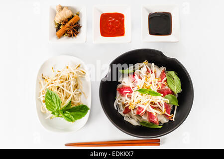 Pho - vietnamesische seltene Rindfleisch Nudelsuppe auf weißem Hintergrund Mit Hoisin-Sauce, Tabasco, Gewürze, Sojabohnensprossen und frischem Basilikum Stockfoto