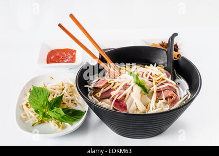 Pho - vietnamesische seltene Rindfleisch Nudelsuppe auf weißem Hintergrund Mit Hoisin-Sauce, Tabasco, Gewürze, Sojabohnensprossen und frischem Basilikum Stockfoto