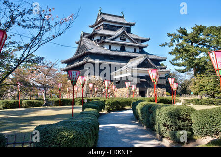 Matsue Castle in Japan. Tagesansicht des Borogata-Stils halten, Tenshu mit frühlingshaften Kirschblütenlaternen vor einem klaren blauen Himmel. Stockfoto