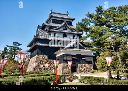 Matsue Castle in Japan. Tagesansicht des Borogata-Stils halten, Tenshu mit frühlingshaften Kirschblütenlaternen vor einem klaren blauen Himmel. Stockfoto