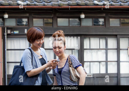 Zwei Frauen stehen im Freien, mit Blick auf Handy. Stockfoto