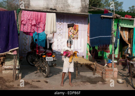 Indien-2014. Orissa. Sambalpur. Schlechte Wohnverhältnisse - jungen halten Baby vor einer Hütte Stockfoto