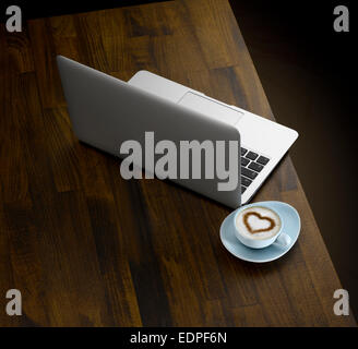 Ein Laptop und eine Tasse Kaffee auf einer hölzernen Tischplatte Stockfoto