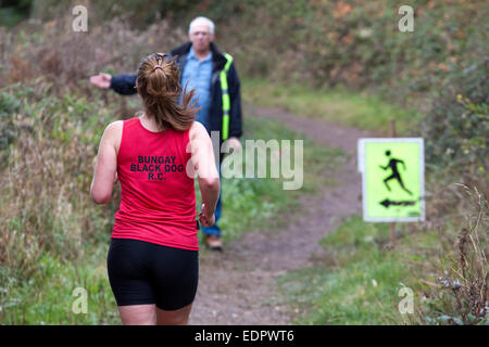 Frau Läufer in rotes Top nähert sich eine gemarshallte Wendung in ein Cross Country Rennen. Stockfoto