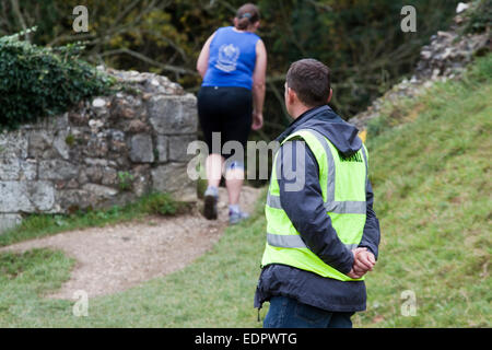 Ein Cross-Country-Rennen-Marschall Uhren einen Frau Läufer vorsichtig nähern sich einen steilen Abstieg Stockfoto