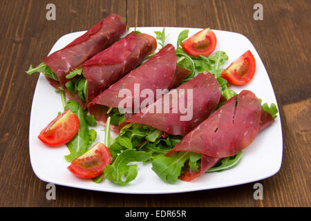 Rollen von Bündnerfleisch auf Platte über Holztisch Stockfoto