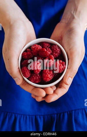 Junge Frau im blauen Kleid hält eine weiße Schüssel mit Himbeeren Stockfoto