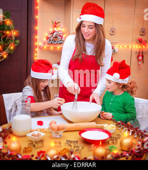 Glückliche Familie kochen für Weihnachten, Mutter mit zwei niedlichen Kinder tragen rote Santa Hüte machen festliches Essen in der Küche Stockfoto