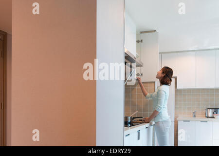 Junge Frau, die im Schrank in der Küche Stockfoto