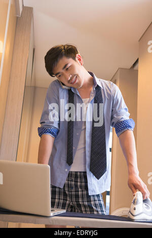 Junger Mann auf dem Handy beim Bügeln Hose Stockfoto