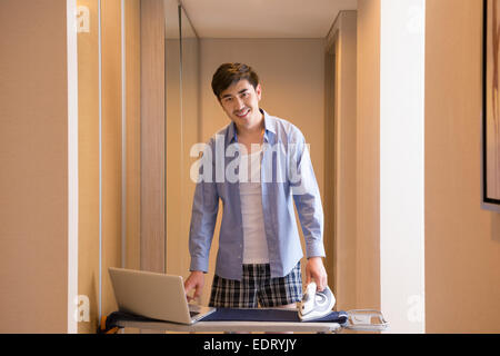 Junger Mann mit Laptop beim Bügeln Hose Stockfoto