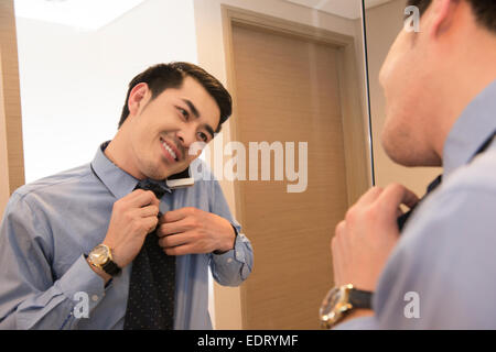 Junger Mann auf dem Handy beim Krawatte anziehen Stockfoto