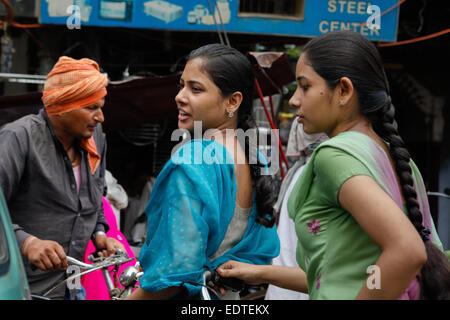 Mädchen, die während eines Verkehrsstaus ein Gespräch führen, während sie in Varanasi, Uttar Pradesh, Indien, Fahrrad fahren Stockfoto