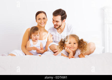 Nette Familie sitzt auf dem Bett in weißen Schlafanzug Stockfoto