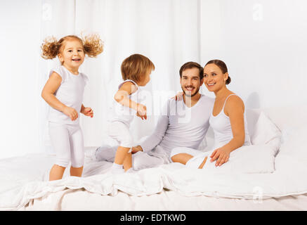 Vater, Mutter und ihre niedlichen Kinder auf weißen Bett Stockfoto