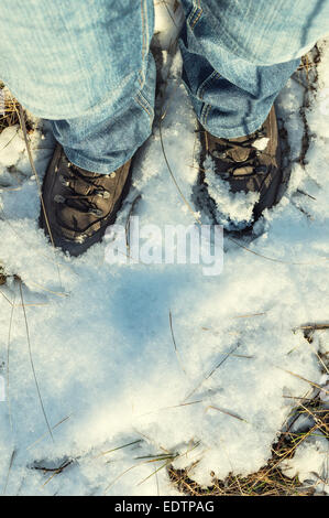 Braune Stiefel mit Schnee zu Fuß auf einem schneebedeckten Feld bedeckt. Stockfoto