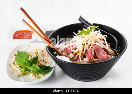 Pho - vietnamesische seltene Rindfleisch Nudelsuppe auf weißem Hintergrund Mit Hoisin-Sauce, Tabasco, Gewürze, Sojabohnensprossen und frischem Basilikum Stockfoto