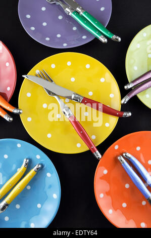 Abendessen-Partei-Tischdekoration mit rot, blau, gelb, Orange, grün und lila hell gepunkteten Teller und Besteck auf schwarzen Tisch Stockfoto