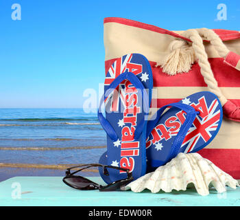Australischen Strand-Szene mit Aussie Sandalen, Strandtasche, Sonnenbrille und Schale mit Blick auf den blauen Ozean. Stockfoto