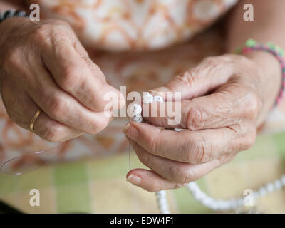 Händen der Seniorin Einfädeln eine Halskette. Hände-Makro-Detail. Stockfoto