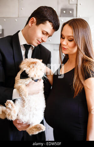 Stilvolle elegante junge Paar erwartet ein Baby. Brünette Frau in schwarzen Cocktailkleid und Mann im Smoking Holding rote flauschige Katze. Stockfoto