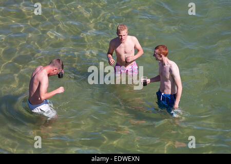 Drei Jungs stehen im Meer mit Getränken in Bournemouth im August Stockfoto